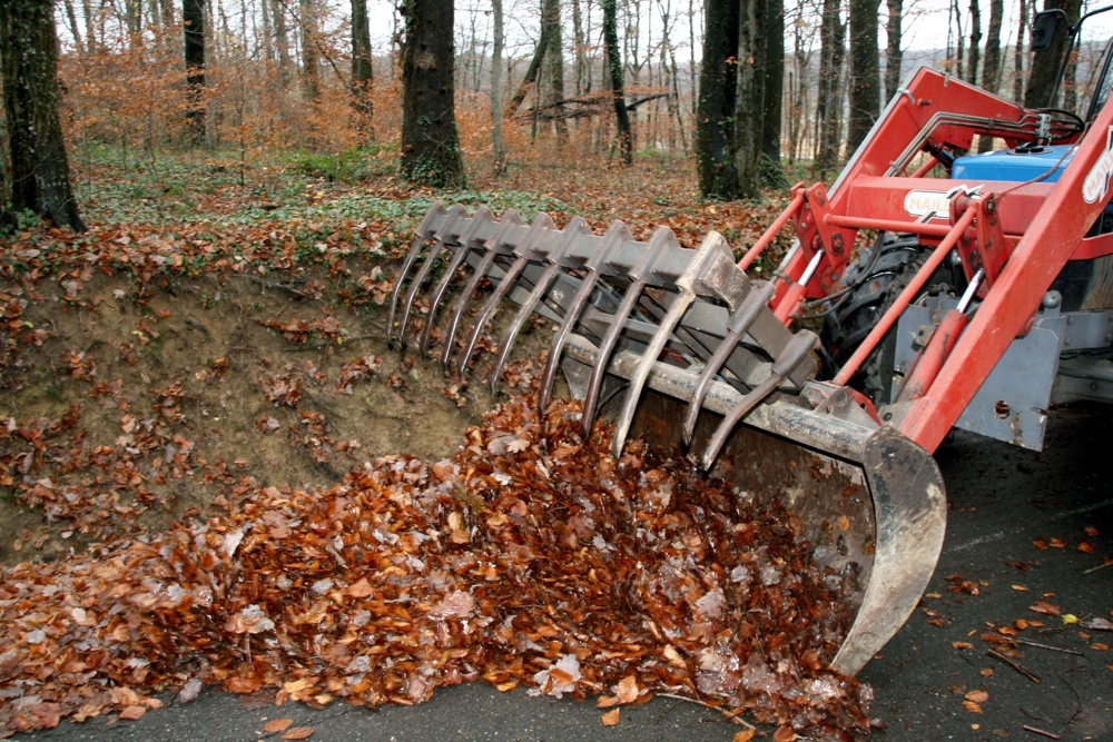 La grosse mâchoire du tracteur qui ramasse les nombreuses feuilles mortes sur un sentier forestier de Waldighoffen